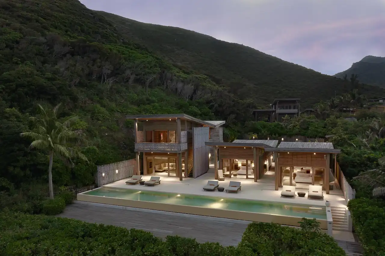 A beachfront four-bedroom pool villa at Six Senses Con Dao at dusk, with its long private pool below the forested hills
