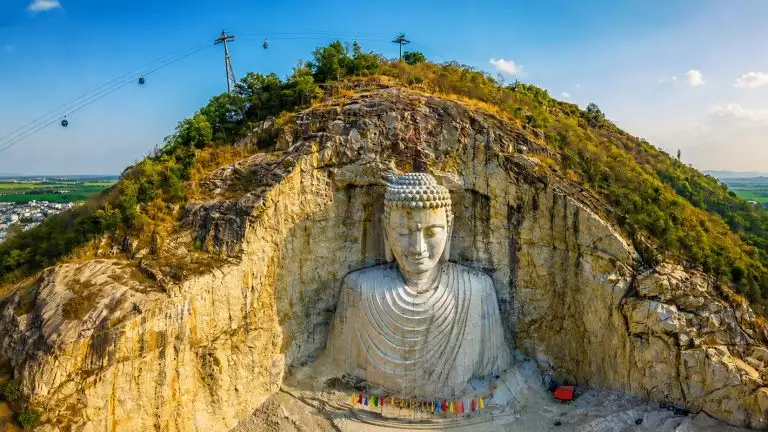 Giant Buddha statue on Núi Sam Mountain in An Giang, Vietnam, surrounded by rocky cliffs and green landscapes.